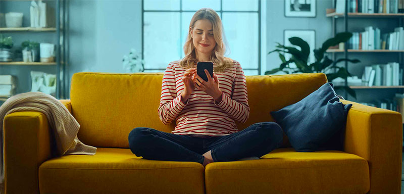 Female Using Smartphone in Stylish Living Room while Sitting on a Cozy Couch Sofa.