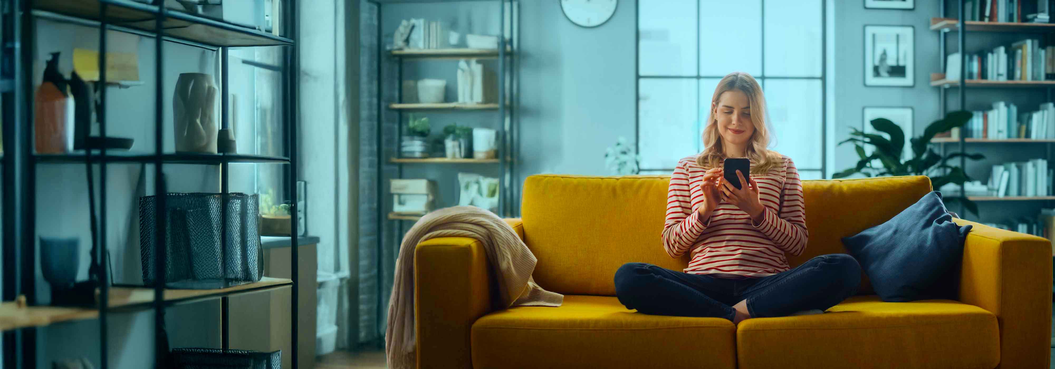 Female Using Smartphone in Stylish Living Room while Sitting on a Cozy Couch Sofa.