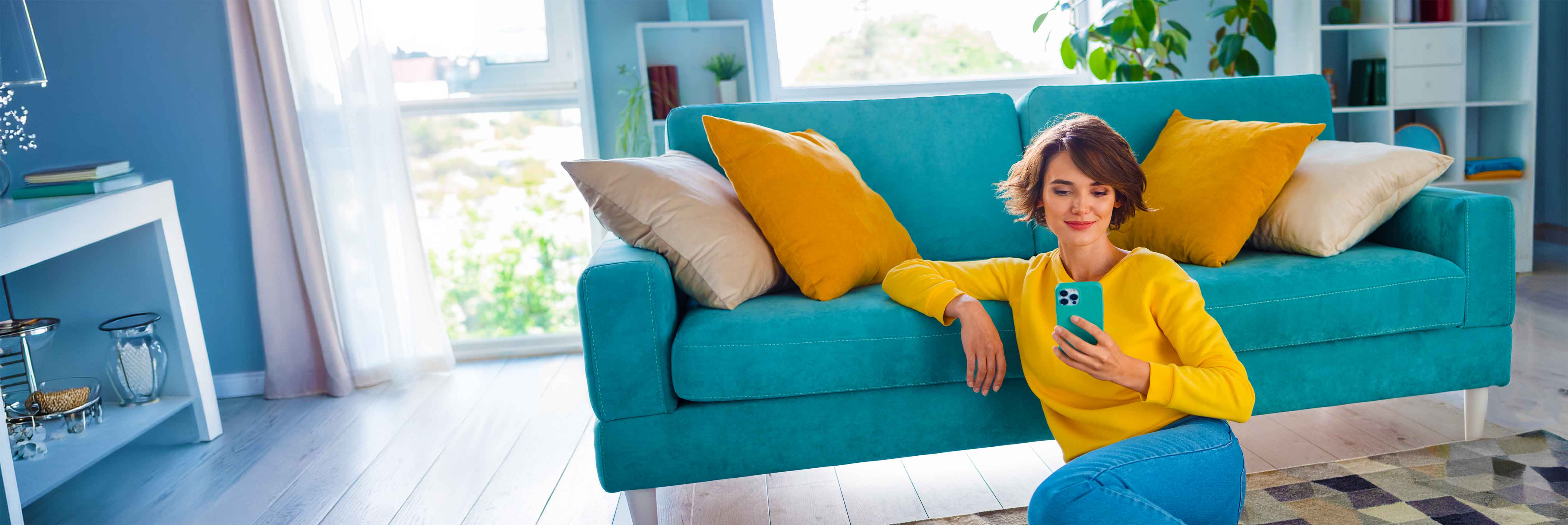 Woman sitting on the floor, leaning on the couch looking at her phone